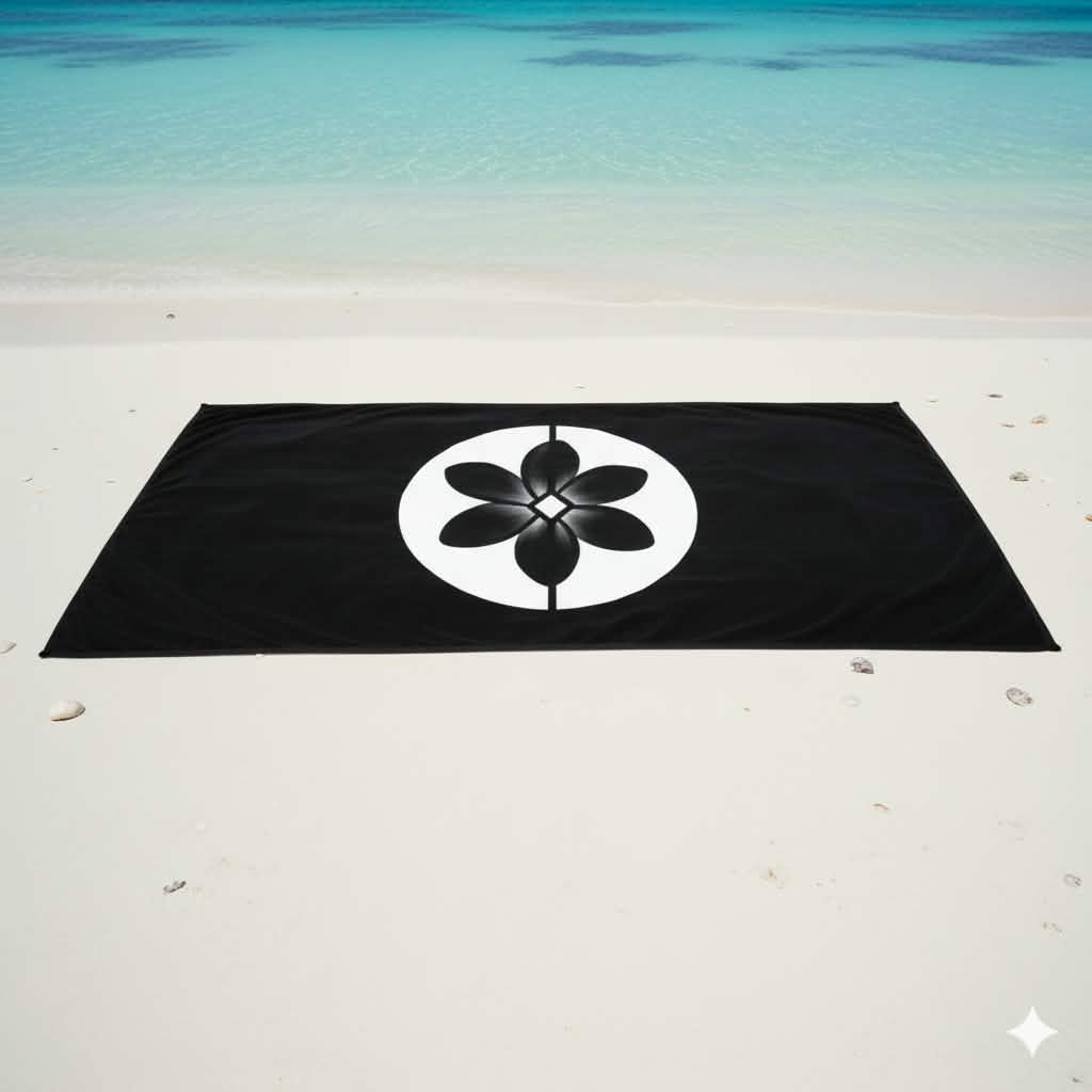 Fleur OEA brodée sur serviette de plage noire, lagon turquoise en arrière-plan